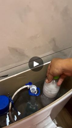 a person is holding a bottle over a sink with water coming from the faucet