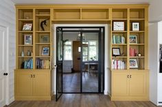 a room with yellow bookshelves and wooden floors in front of a door that leads to another room