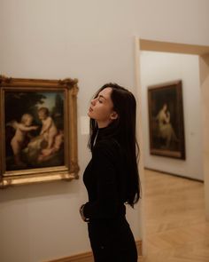 a woman standing in front of two paintings on the wall and looking up at it