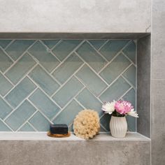 two vases with flowers sit on a shelf in front of a blue tiled wall