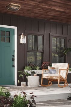 a wooden rocking chair sitting on the porch next to a green door and potted plants