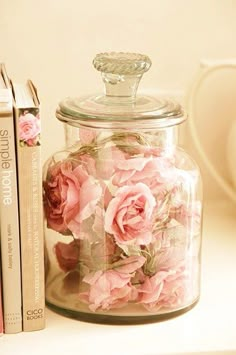 a glass jar with pink flowers sitting next to two books on a white table top