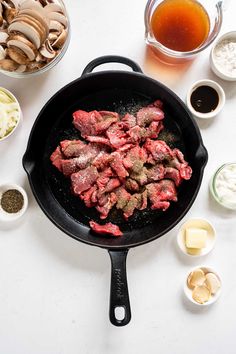 steak cooking in a skillet with ingredients around it on a white counter top,