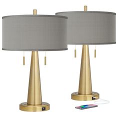 two gold metal lamps with grey shades on each one and a phone charging in the other