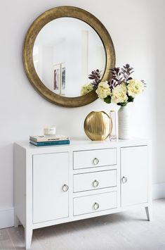 a white dresser with flowers and a round mirror