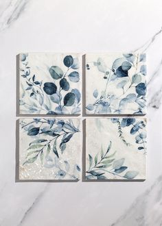 four square tiles with blue and green leaves on them sitting on a marble countertop