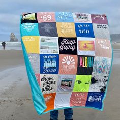 a person standing on the beach holding up a colorful blanket that has various stickers all over it