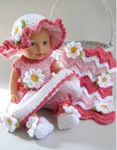 a baby doll is sitting next to a basket with a crocheted blanket and booties