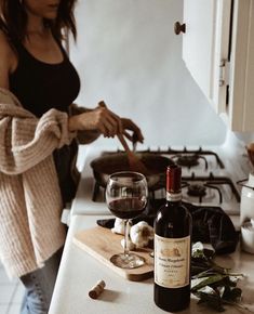 a woman standing next to a bottle of wine on top of a counter with a knife