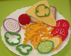 crocheted food on a white plate with green and red trimmings sitting on a green surface