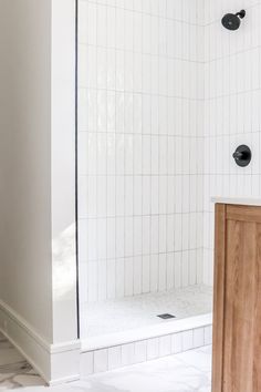 a bathroom with white tile and wooden cabinet next to the bathtub, shower head and door