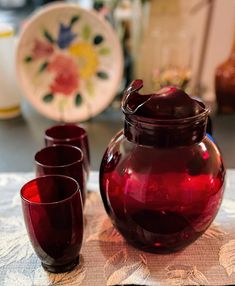 a red vase sitting on top of a table next to two glasses and a pitcher