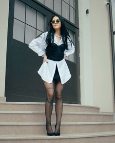 a woman in black and white outfit standing on steps with her hands behind her back