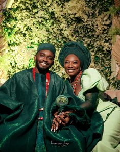 a man and woman sitting next to each other in front of a wall covered with plants