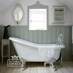 a white bath tub sitting inside of a bathroom next to a sink and mirror on top of a wooden floor