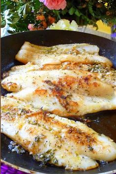 two pieces of fish are cooking in a frying pan on a table with flowers