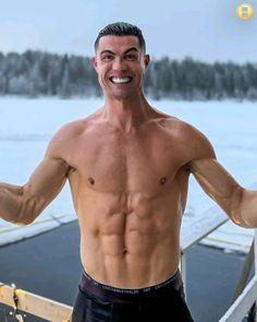 a man with no shirt on standing next to a body of water and holding his arms out