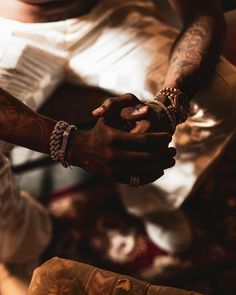 a man with tattoos and bracelets on his arm holding onto another mans hand while sitting down