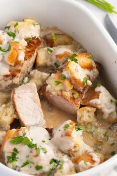 a white bowl filled with meat and potatoes covered in gravy on top of a table