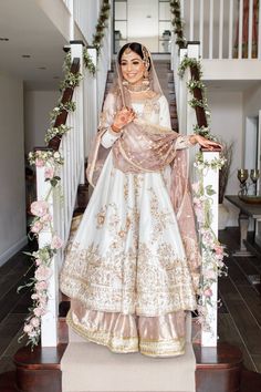 a woman in a white and gold bridal gown standing on stairs with flowers around her