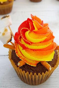 a cupcake with orange frosting and marshmallows on top, sitting on a table