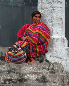 a woman sitting on the steps with a colorful blanket over her shoulders and purse in front of her