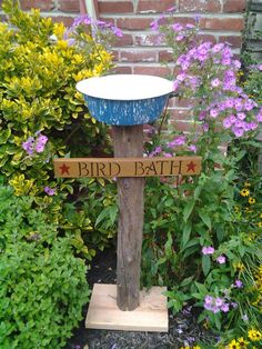 a bird bath sitting on top of a wooden pole in front of flowers and bushes