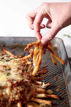 someone is dipping cheese on top of french fries in a pan with sauce and parmesan