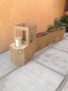 a cardboard train is sitting on the sidewalk next to a planter and potted plants