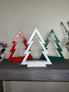 three wooden christmas trees sitting on top of a table next to vases and flowers