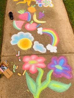 sidewalk chalk art with flowers, clouds and rainbows painted on the pavement next to it