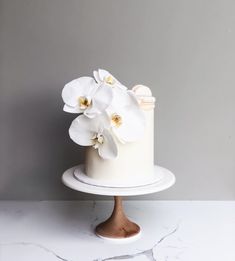 there is a white cake with flowers on the top and bottom, sitting on a marble stand