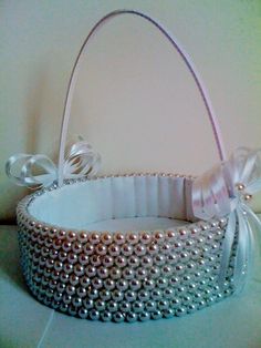 a white basket with pearls and bows on the inside is sitting on a table next to a wall