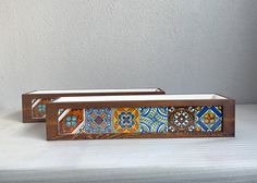 two wooden trays sitting on top of a white bed covered in blue and orange tiles