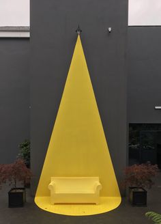 a yellow bench sitting in front of a building with a triangle on it's side