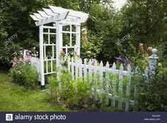 a white picket fence surrounded by flowers and greenery