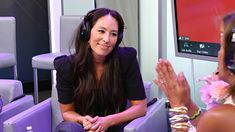 a woman wearing headphones sitting in front of a tv screen and another person clapping