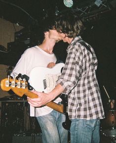 two young men standing next to each other while playing guitars