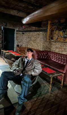 a man sitting on a bench in a room with brick walls and leather couches