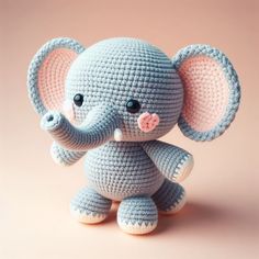 a small crocheted elephant sitting on top of a pink surface with its trunk in the air