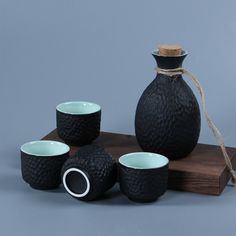 three black vases and four cups on a wooden tray with string tied to them