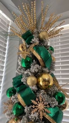 a christmas tree with green and gold ornaments on it's top, in front of a window