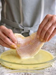 a person in an apron is preparing fish on a plate with sauces and butter