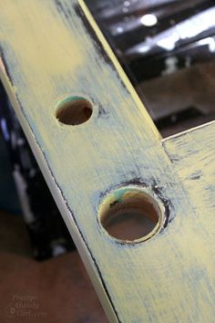 two holes in the side of a yellow wooden bench that has been painted blue and white