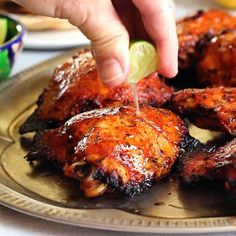 a person dipping a lime into some chicken wings on a plate with other food items in the background