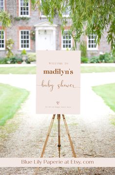 a welcome sign for a baby shower in front of a large brick building with trees and grass