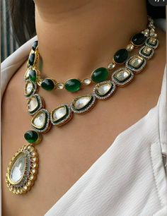 a woman wearing an elaborate necklace with green and white stones on the bottom, along with other jewelry pieces