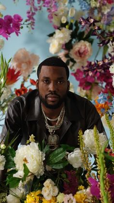 a man sitting in front of flowers with his hands on his hips and looking at the camera