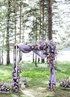 an outdoor wedding ceremony setup with purple flowers and lavender draping on the arch