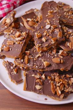 a white plate topped with pieces of chocolate covered in nuts and pecans on top of a wooden table